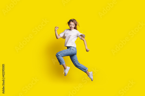 Crazy woman is jumping in a yellow studio wall smiling at camera gesturing a run