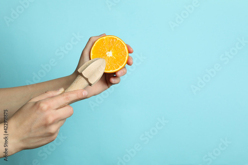 Female hands hold orange and juicer on blue background