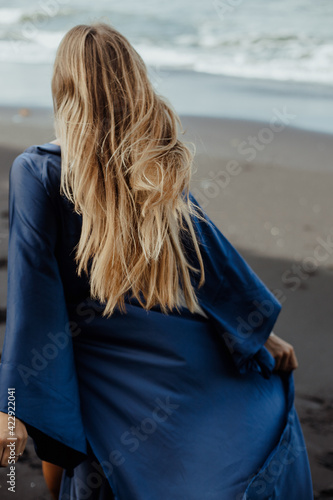 Photoshoot of a blonde girl in a blue dress on the Bali beach with black sand