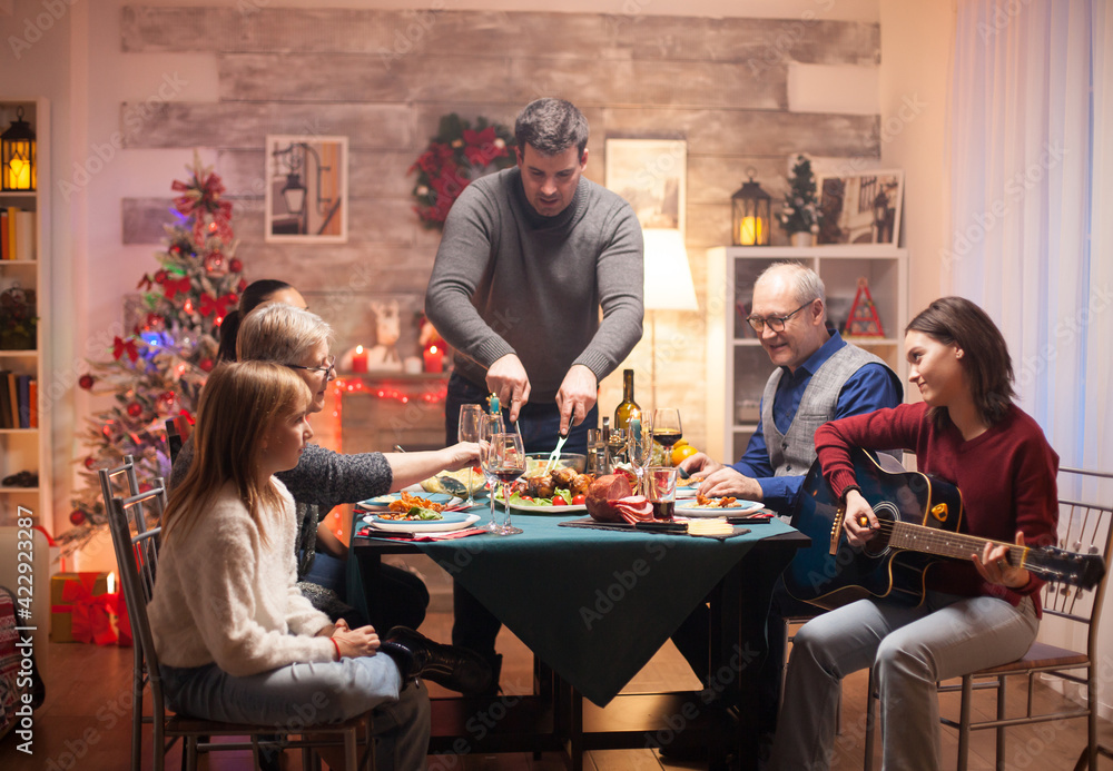 Cheerful girl singing on guitar while his father is slicing the chicken at christmas family celebration. Cheerful girl singing on guitar while his father is slicing the chicken at christmas family celebration.