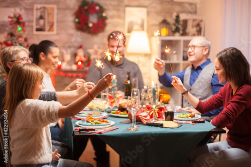 Cheerful senior man at christmas family dinner holding hand fireworks.