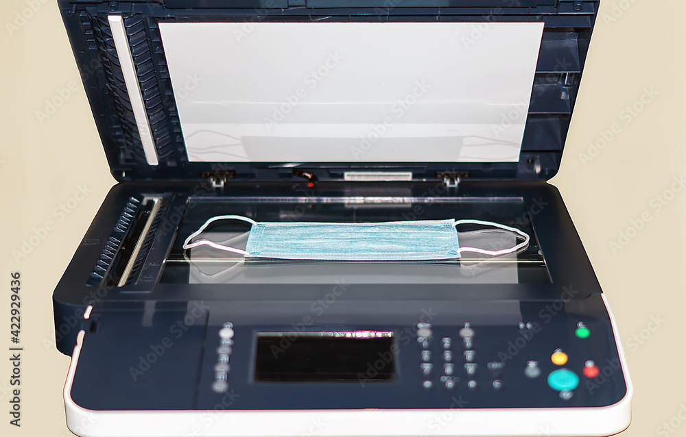A medical surgical mask is placed in a copy machine for scanning and distribution. A funny or ironic concept about the shortage of disposable masks on sale in stores and pharmacies. A medical surgical mask is placed in a copy machine for scanning and distribution. A funny or ironic concept about the shortage of disposable masks on sale in stores and pharmacies.