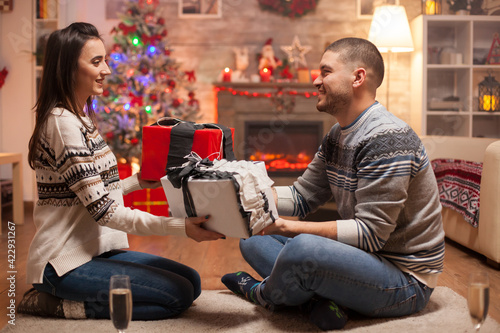 Cheerful boyfriend giving his girlfriend a gift on christmas day. Warm fireplace.