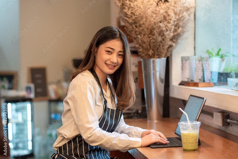 Small business owner, an Asian woman working using tablet and a coffee mug at a cafe. Looking at the camera. Small business owner, an Asian woman working using tablet and a coffee mug at a cafe. Looking at the camera.