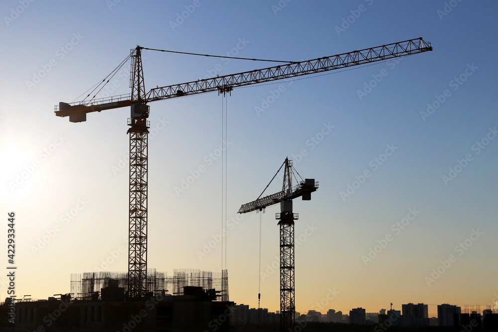 Silhouettes of construction cranes and buildings on sunrise background. Housing construction, apartment block in city