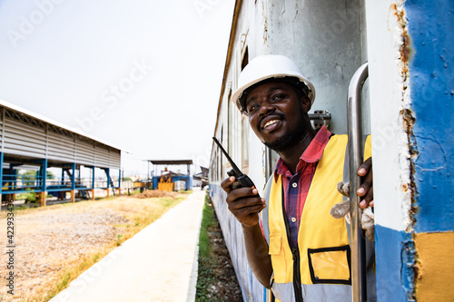 Portrait of Africa American man engineering holding railing and with wear hardhat in front of train station. Preparation for train mechanical operation. Technician man