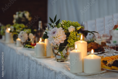 Beautiful decor with candles and fresh cut flowers on the wedding table of newlyweds. Wedding table.