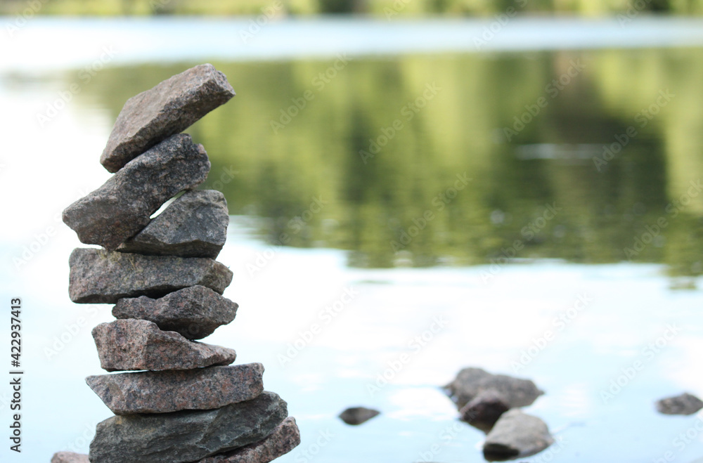 tower built of stones stacked on top of each other on the edge of a pond, green background with space for text