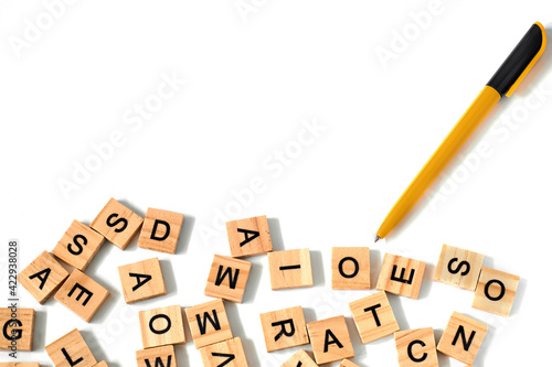 Top view of yellow-black pen and square wooden tiles with the English alphabet scattered on a white background with space for text. The concept of thinking development  grammar.