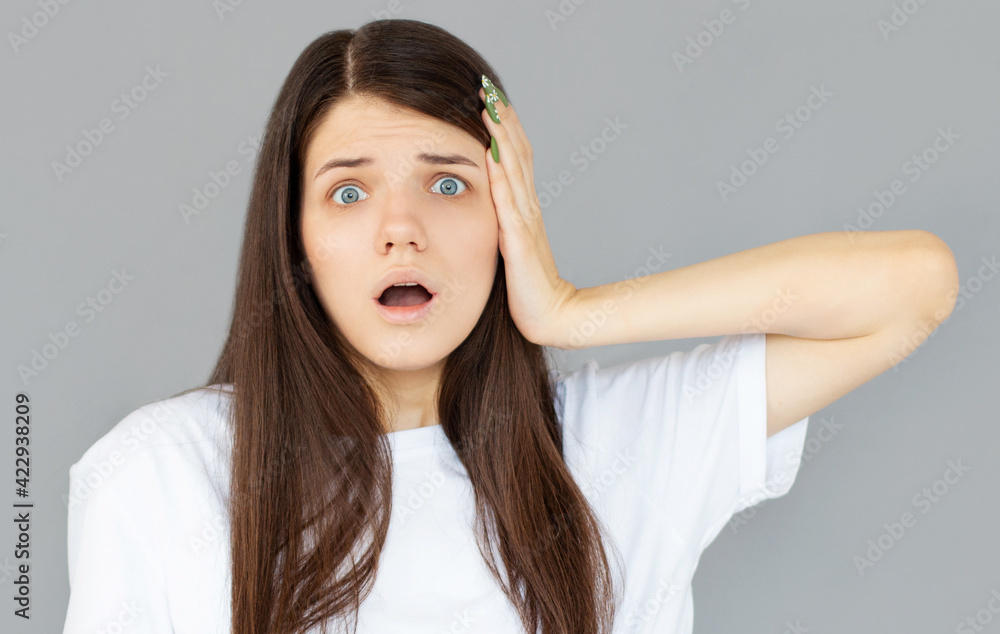 Shocked amazed young woman with hands on head standing and shouting over gray background Shocked amazed young woman with hands on head standing and shouting over gray background