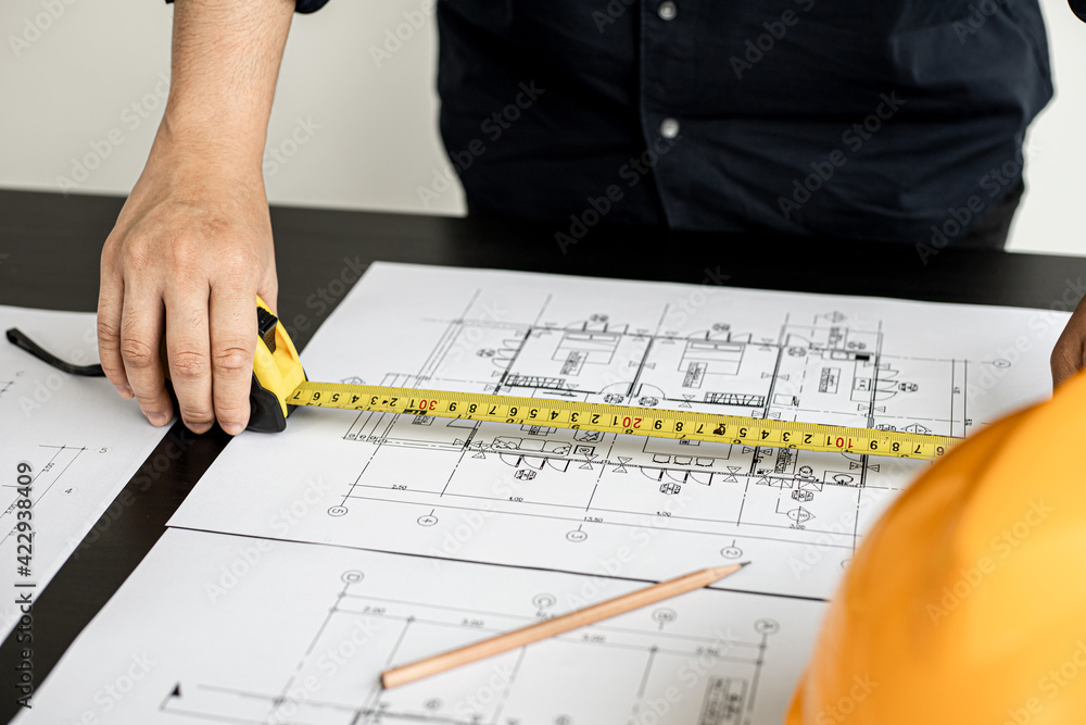 An engineer is using a tape measure to measure the plans of the house that he designs, the drafts the house drawings to build the correct standard. Engineer concept. An engineer is using a tape measure to measure the plans of the house that he designs, the drafts the house drawings to build the correct standard. Engineer concept.