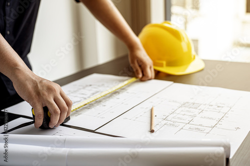 An engineer is using a tape measure to measure the plans of the house that he designs, the drafts the house drawings to build the correct standard. Engineer concept.