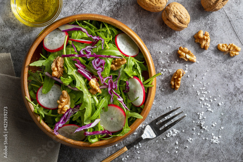 Appetizing and healthy low calorie salad with arugula, radishes, red cabbage and walnuts. In a wooden bowl and homemade look. Mediterranean diet. Mediterranean diet. Top view and copy space.