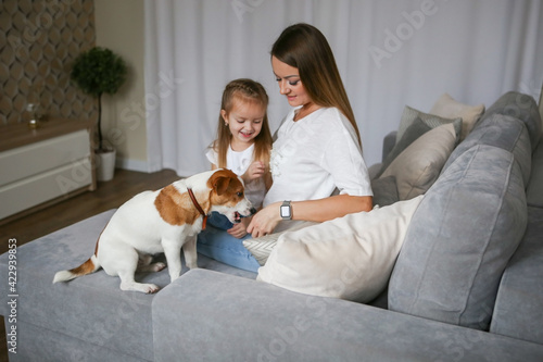 Woman in light clothes have fun with cute baby girl. Young mom with her daughter playing with Jack Russell Terrier dog. Family and pet at home.