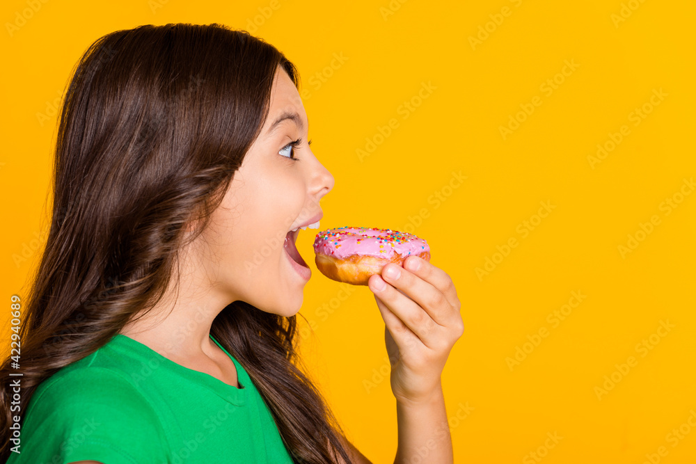 Profile side photo of hungry happy little girl eat sweets donut isolated on shine yellow color background Profile side photo of hungry happy little girl eat sweets donut isolated on shine yellow color background