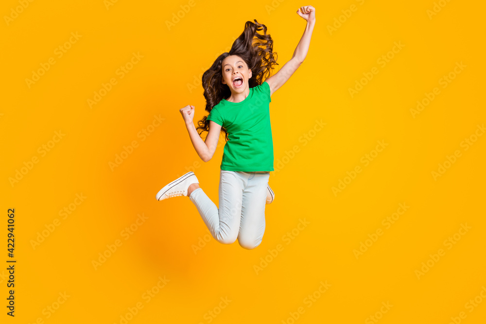 Full size photo of happy screaming happy excited little girl jumping raise fists in victory isolated on yellow color background Full size photo of happy screaming happy excited little girl jumping raise fists in victory isolated on yellow color background