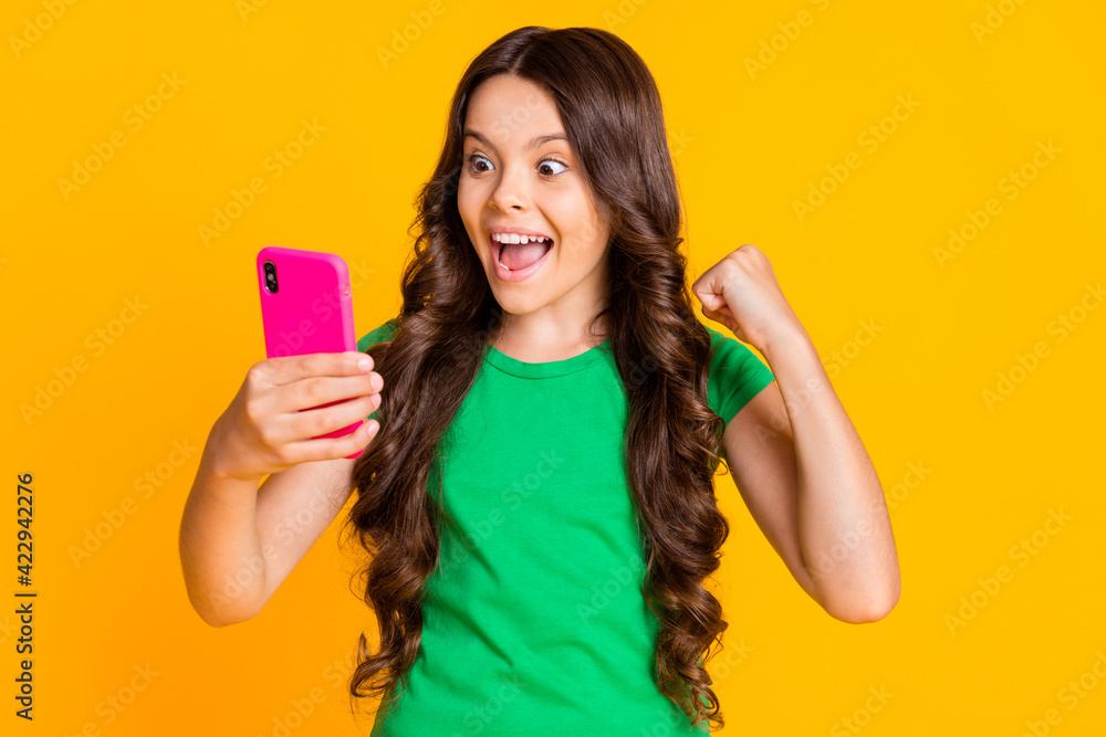 Photo of young funky crazy excited smiling cheerful girl winning in online lottery in phone isolated on yellow color background Photo of young funky crazy excited smiling cheerful girl winning in online lottery in phone isolated on yellow color background