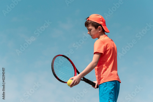 Child boy tennis player with racket and ball is focused and concentrated prepares to serve ball in match. Kids sport tennis game. Sports physical activity of children. Background copy space © Elena