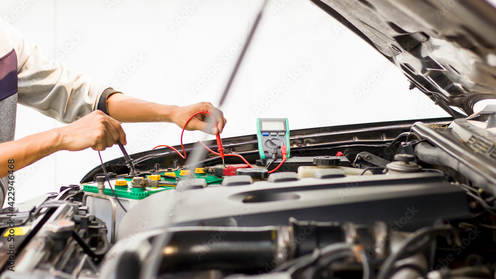 A technician is checking the car battery for availability.; A technician is checking the car battery for availability.;