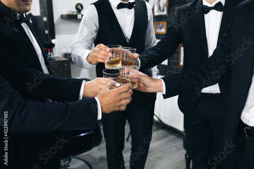 Promising young men celebrate and drink whiskey. Best men with glasses filled up with alcohol drinks dressed in formal attires.