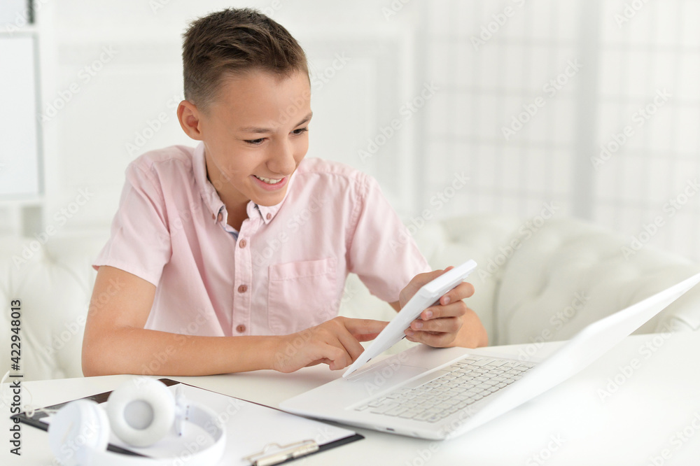 Cute boy using calculator while sitting at table Cute boy using calculator while sitting at table