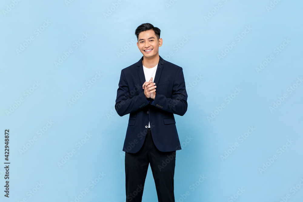 Smiling young handsome southeast Asian man clapping hands impressively in light blue studio isolated background Smiling young handsome southeast Asian man clapping hands impressively in light blue studio isolated background