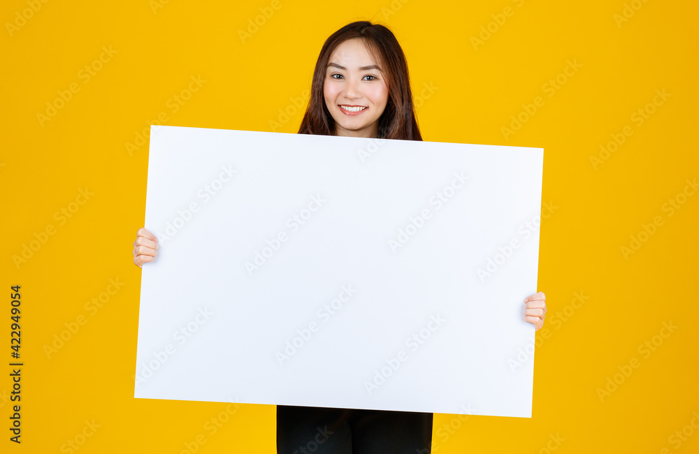Cute and pretty curly hair Asian female brunette holding white blank board poses to camera with a joyful for advertising and banner use purpose, studio shot isolated on bright yellow background Cute and pretty curly hair Asian female brunette holding white blank board poses to camera with a joyful for advertising and banner use purpose, studio shot isolated on bright yellow background