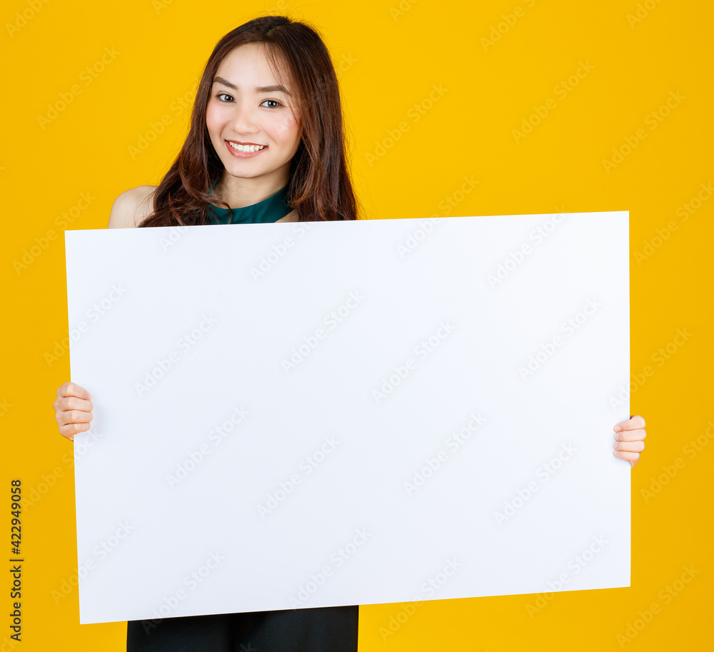 Cute and pretty curly hair Asian female brunette holding white blank board poses to camera with a joyful for advertising and banner use purpose, studio shot isolated on bright yellow background Cute and pretty curly hair Asian female brunette holding white blank board poses to camera with a joyful for advertising and banner use purpose, studio shot isolated on bright yellow background