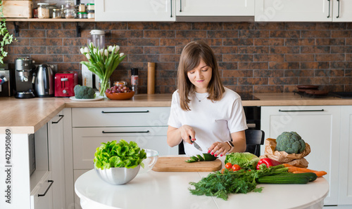 Brunette Woman in white t-shirt preparing vegetable salad in the kitchen at home  Wife Cutting ingredients on table. Healthy Food  Vegan Salad. Dieting Concept.
