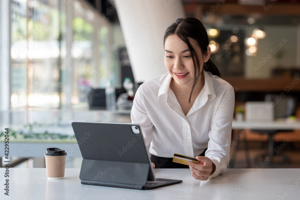 Asian  businesswoman beauty smiling holding credit card card shop online using a tablet at the office.