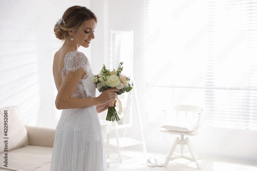 Gorgeous bride in beautiful wedding dress holding bouquet in room. Space for text Gorgeous bride in beautiful wedding dress holding bouquet in room. Space for text