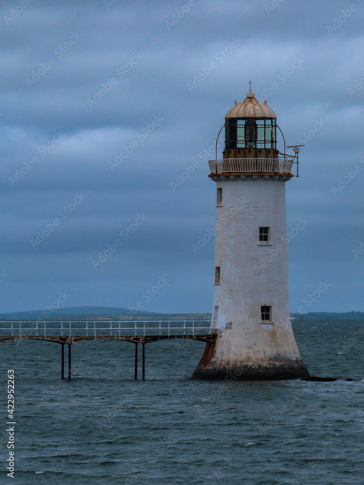 white lighthouse in ocean with dark cloudy sky