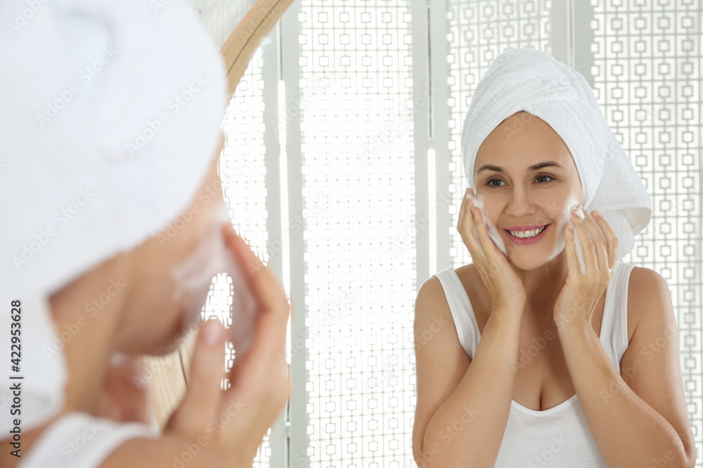 © New Africa - Happy mature woman applying cleansing foam onto face near mirror in bathroom © New Africa - Happy mature woman applying cleansing foam onto face near mirror in bathroom