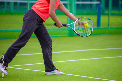 girl in a red T-shirt plays tennis on the grass court