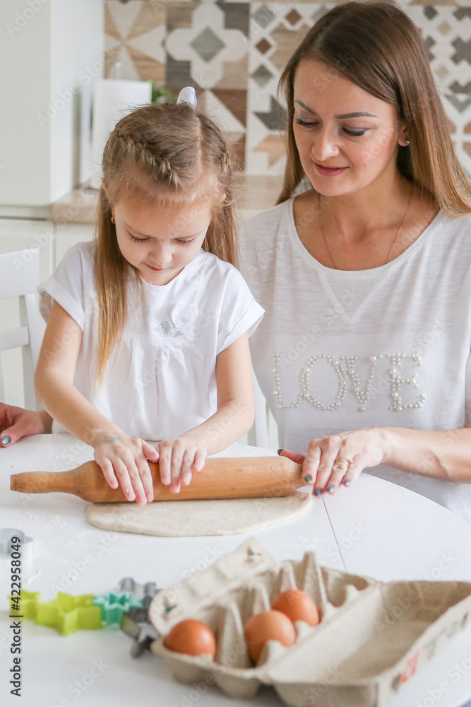 Happy mom and daughter prepare dough together using rolling pin, smiling young mom, charming girl prepare cookies, buns in the kitchen. The concept of a friendly family preparing for Easter Happy mom and daughter prepare dough together using rolling pin, smiling young mom, charming girl prepare cookies, buns in the kitchen. The concept of a friendly family preparing for Easter