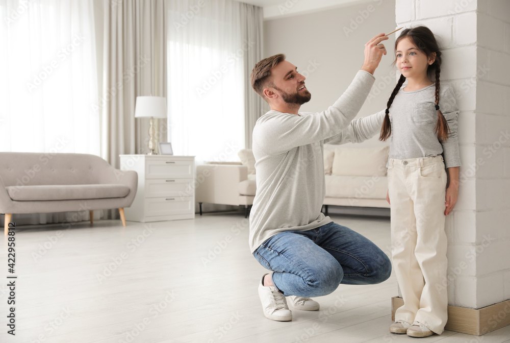 Father measuring daughter's height near white brick pillar at home, space for text Father measuring daughter's height near white brick pillar at home, space for text