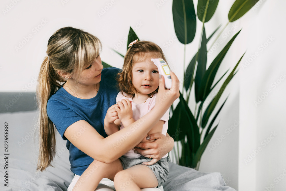 A worried mother checks her daughter's temperature with an electronic thermometer A worried mother checks her daughter's temperature with an electronic thermometer