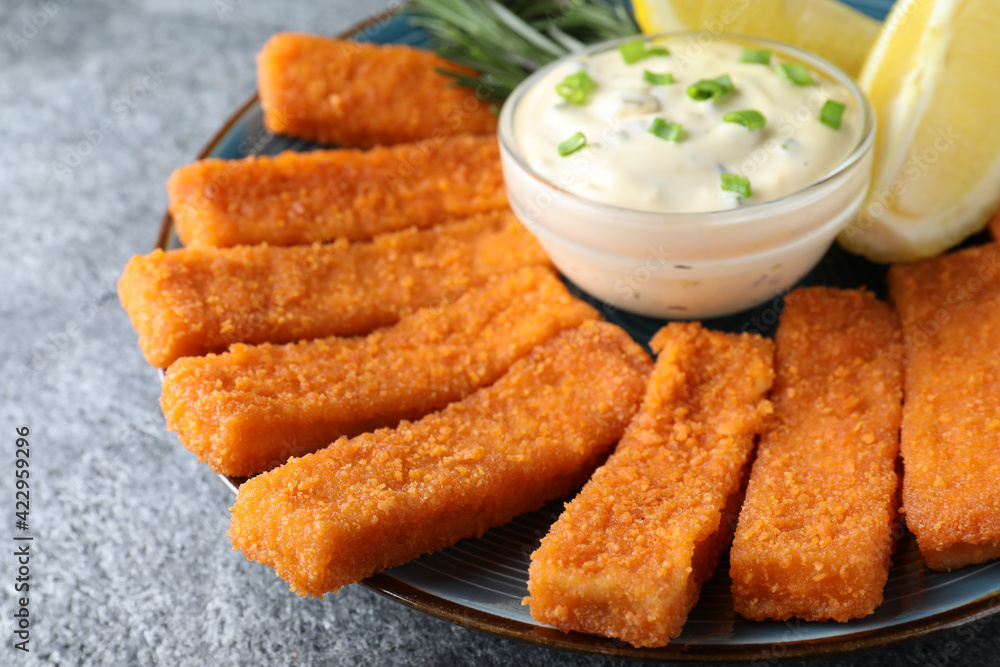 Fresh breaded fish fingers, sauce and lemon served on grey table, closeup Fresh breaded fish fingers, sauce and lemon served on grey table, closeup
