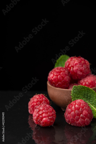 Top view of raspberries and mint leaves in bowl, selective focus, on black slate with reflection, vertical, with copy space