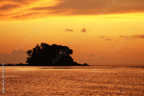 Sunset on a beach, silhouette of tropical island with palm trees in dark sea. Dramatic orange sky with clouds, romantic vacation concept