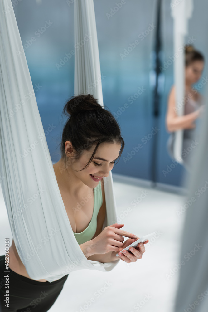 Cheerful woman using mobile phone during fly yoga training Cheerful woman using mobile phone during fly yoga training