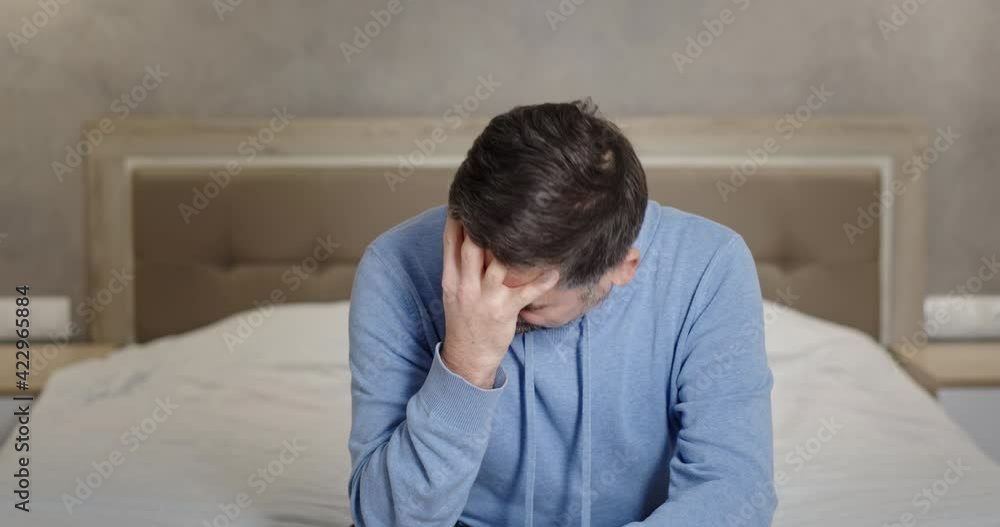 Desperate middle aged man crying on bed. Stressed mature male taking off glasses and rubbing face while sitting on bed and crying in despair at home Desperate middle aged man crying on bed. Stressed mature male taking off glasses and rubbing face while sitting on bed and crying in despair at home