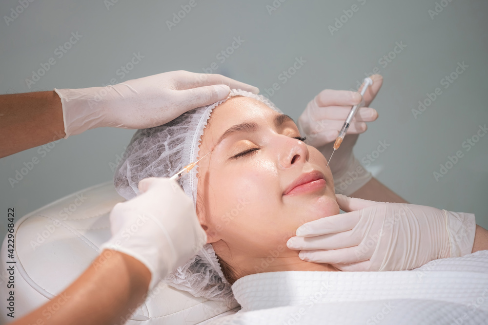Doctor wearing glove and use syringe making injection to beautiful woman. Plastic surgery in the clinic. Cosmetology and skin care concept. Lightening and smoothing wrinkles on the face skin