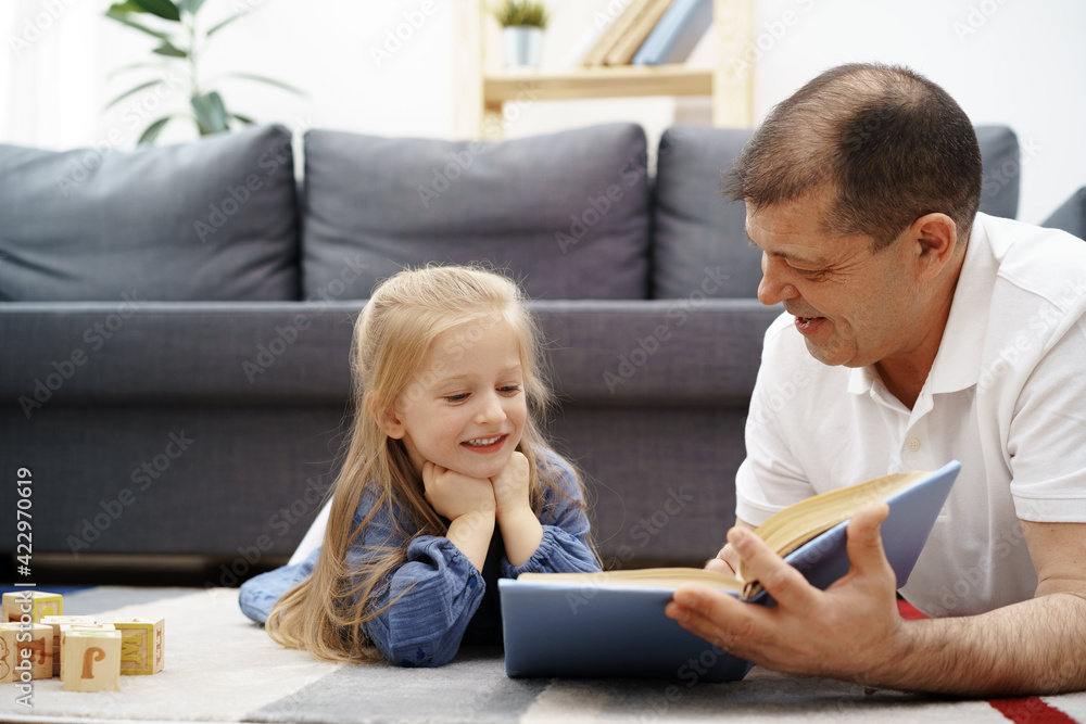 Grandfather reading a book to his little graddaughter in living room Grandfather reading a book to his little graddaughter in living room