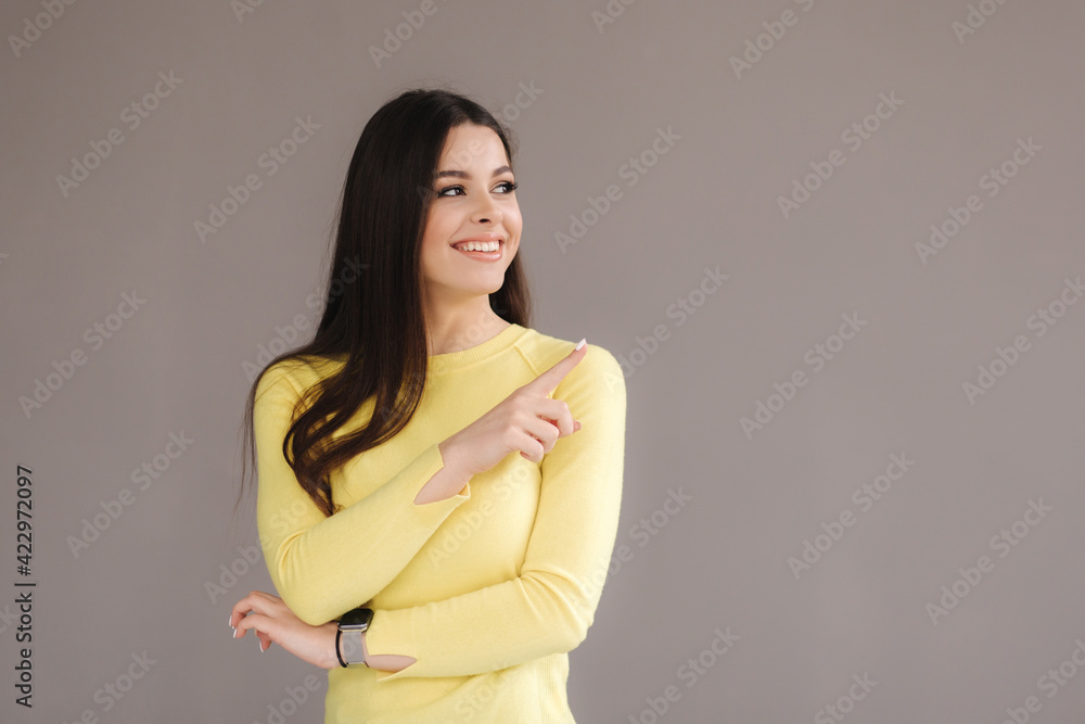 Portrait of attractive woman in yellow sweatshirt point the finger at place for text. Female on grey background Portrait of attractive woman in yellow sweatshirt point the finger at place for text. Female on grey background