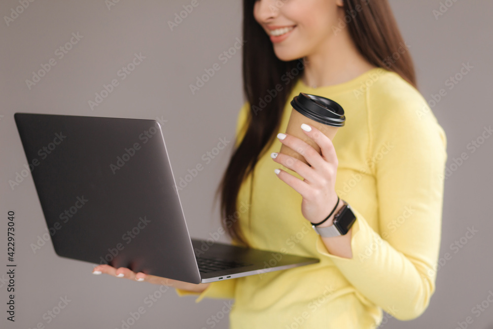 Middle selection of woman in yellow sweatshirt using laptop and drink coffee on gray background. Place for text Middle selection of woman in yellow sweatshirt using laptop and drink coffee on gray background. Place for text