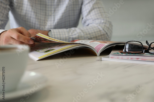 Man reading magazine at white table, closeup