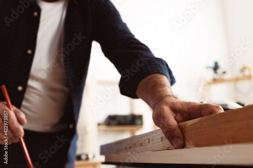 Carpenter makes pencil marks on a wood plank