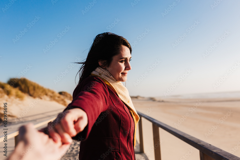 young caucasian woman relaxing at the beach at sunset. Holding hands with camera, follow me. Holidays and relaxation concept
