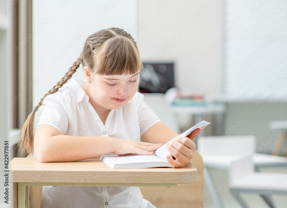 Young girl with syndrome down reads a book at school. Education for disabled children concept Young girl with syndrome down reads a book at school. Education for disabled children concept